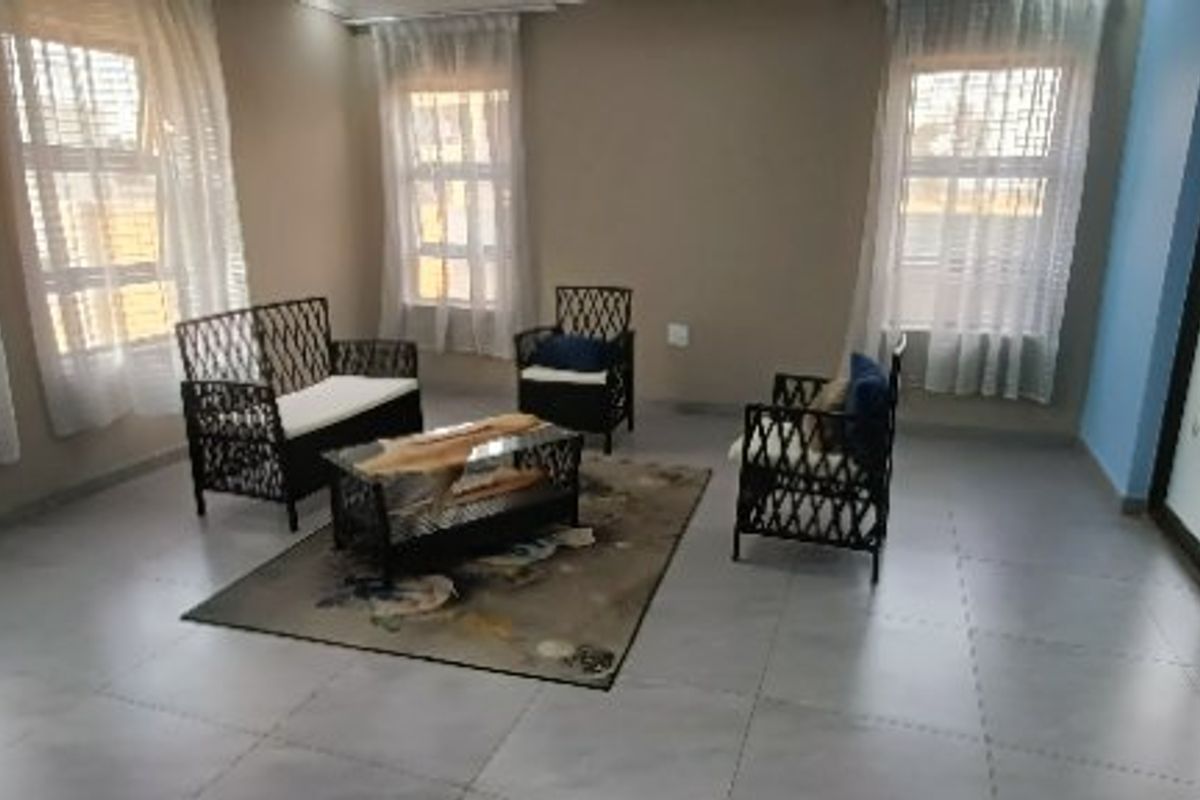 A bright living room featuring large windows, tiled flooring, and sliding glass doors, offering a clean and neutral space for relaxation.