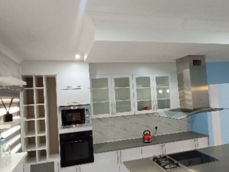 Modern kitchen featuring white cabinetry, stone countertops, built-in oven and microwave, stainless steel extractor fan, and glass-fronted display cabinets.