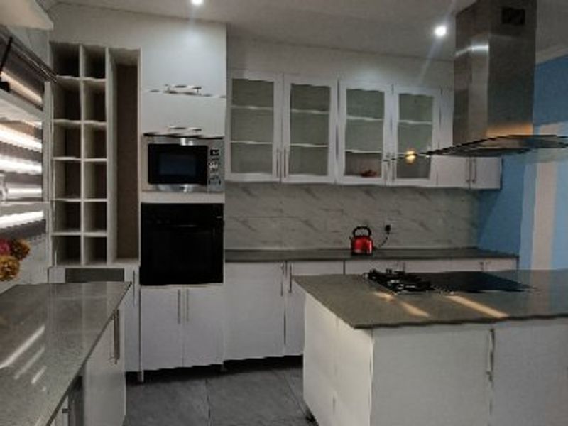 Modern kitchen featuring white cabinetry, stone countertops, a central island with a sink, built-in oven, microwave, and a stainless steel extractor fan.