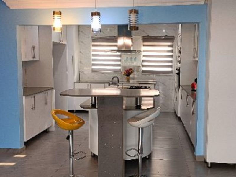 A functional kitchen featuring white cabinetry, a central island with breakfast bar seating, modern pendant lighting, and tiled flooring.