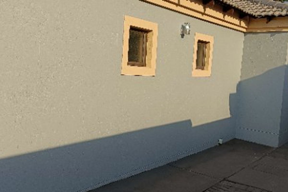 A view of the rear exterior facade featuring a textured wall finish, tiled roof, and a paved walkway along the side of the house.