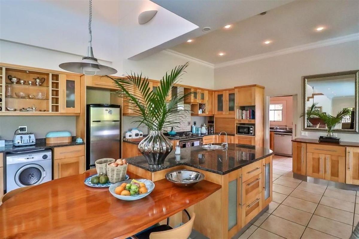 Spacious kitchen featuring light wood cabinetry, granite countertops, a central island with breakfast bar, and integrated appliances, offering a functional and warm cooking space.