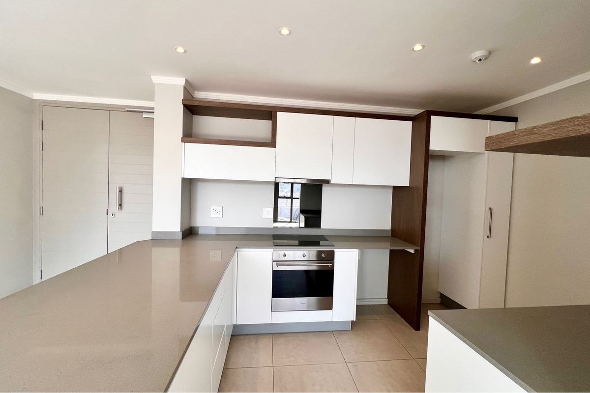 Modern kitchen featuring sleek white cabinetry, stone countertops, integrated oven, and electric hob, offering a clean and functional culinary space.
