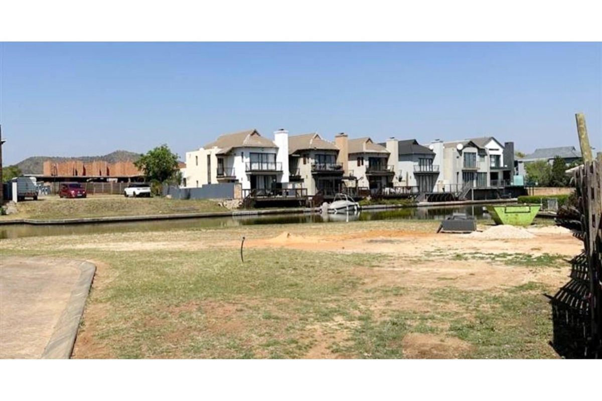 A vacant residential plot featuring canal frontage with views of established waterfront properties in a developed estate setting.