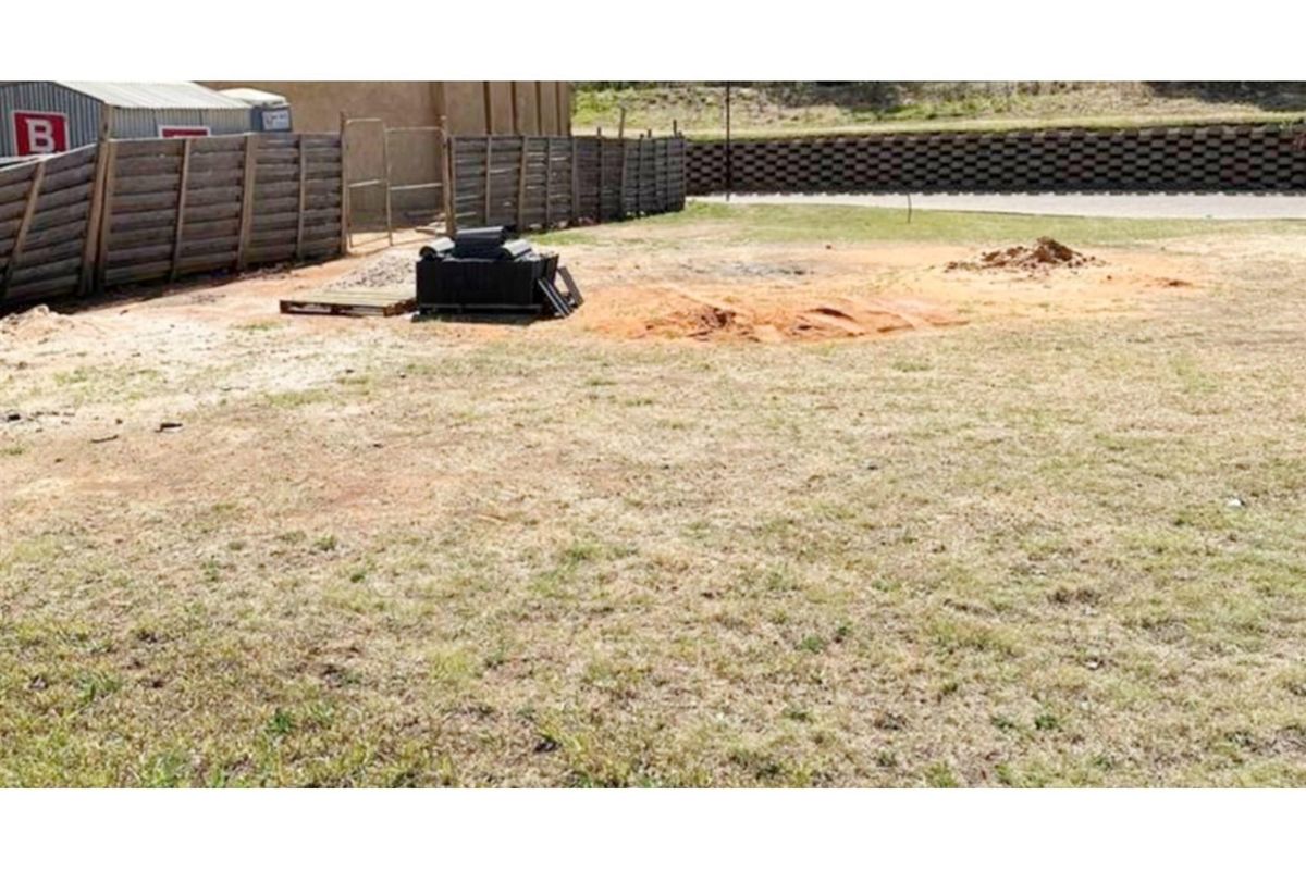 A vacant residential plot featuring a grassed area, wooden perimeter fencing, and a retaining wall at the rear boundary.