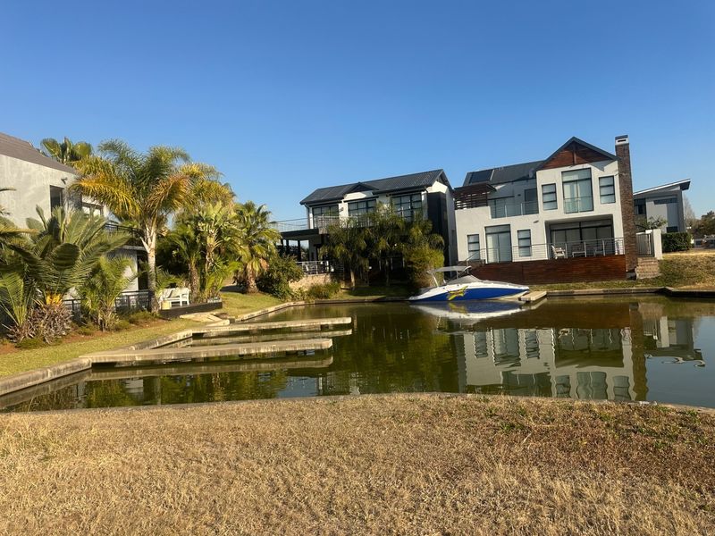 A scenic view of a waterfront residential property featuring a private jetty, landscaped garden, and modern multi-story homes with balcony access.