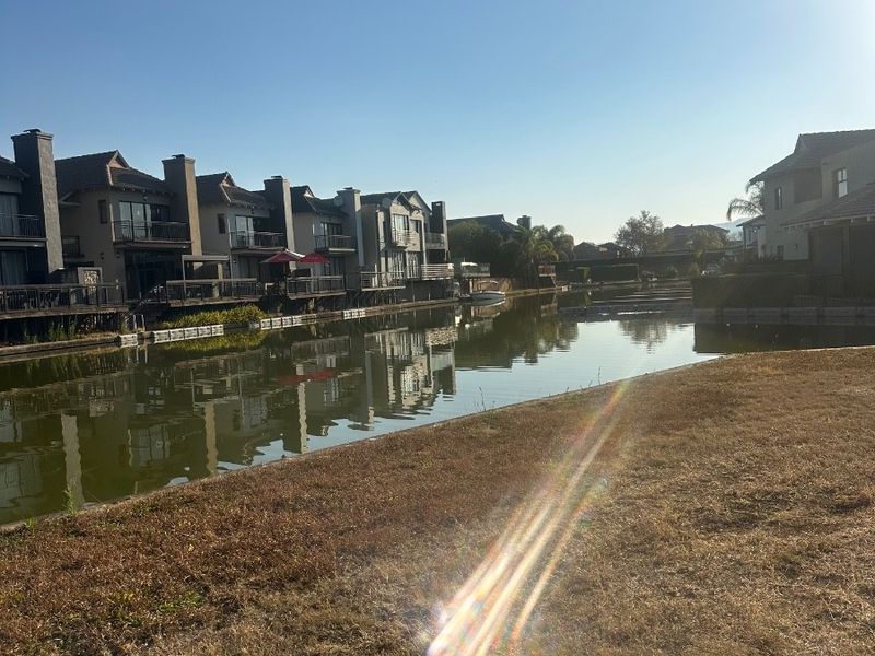 A scenic view of a residential canal with waterfront properties and landscaped banks under a clear blue sky.