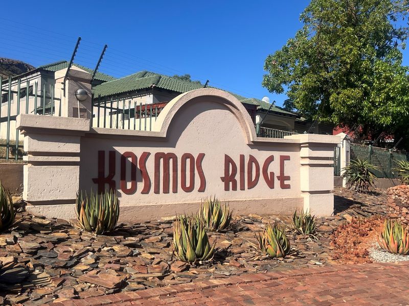 Entrance signage for the Kosmos Ridge residential estate, featuring a masonry wall, landscaped rock garden, and perimeter security fencing.