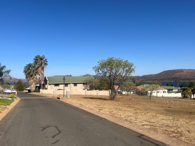 A view of the residential street and surrounding landscape, showcasing the vacant land plot with established trees and distant mountain views.