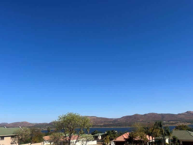 A scenic elevated view overlooking a residential neighborhood with a lake and mountain range in the background.