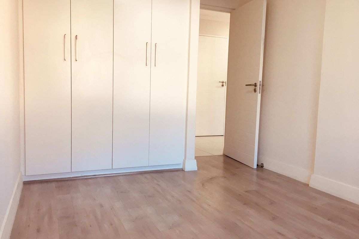 A bright, empty bedroom featuring light wood-look laminate flooring and built-in white cabinetry with modern handles.