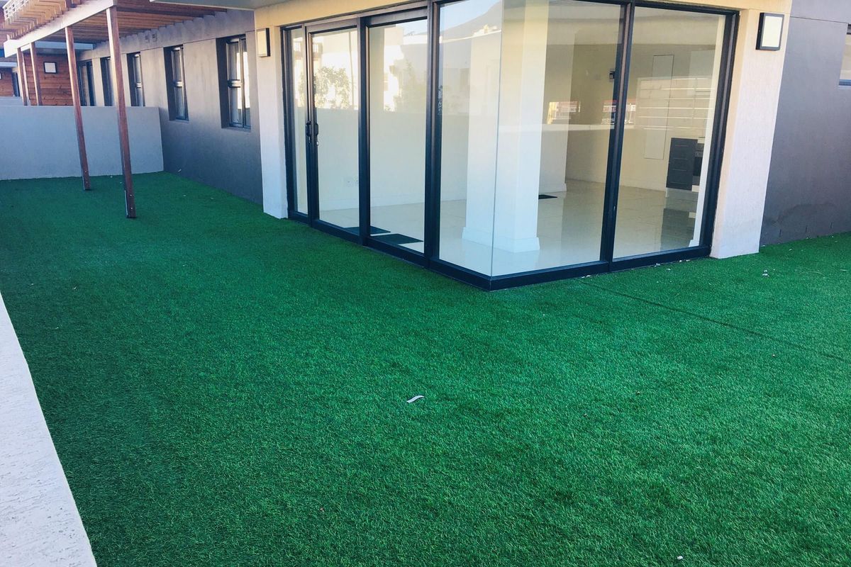 A well-maintained rear garden area featuring artificial turf, a wooden pergola structure, and large glass sliding doors leading into the interior living space.