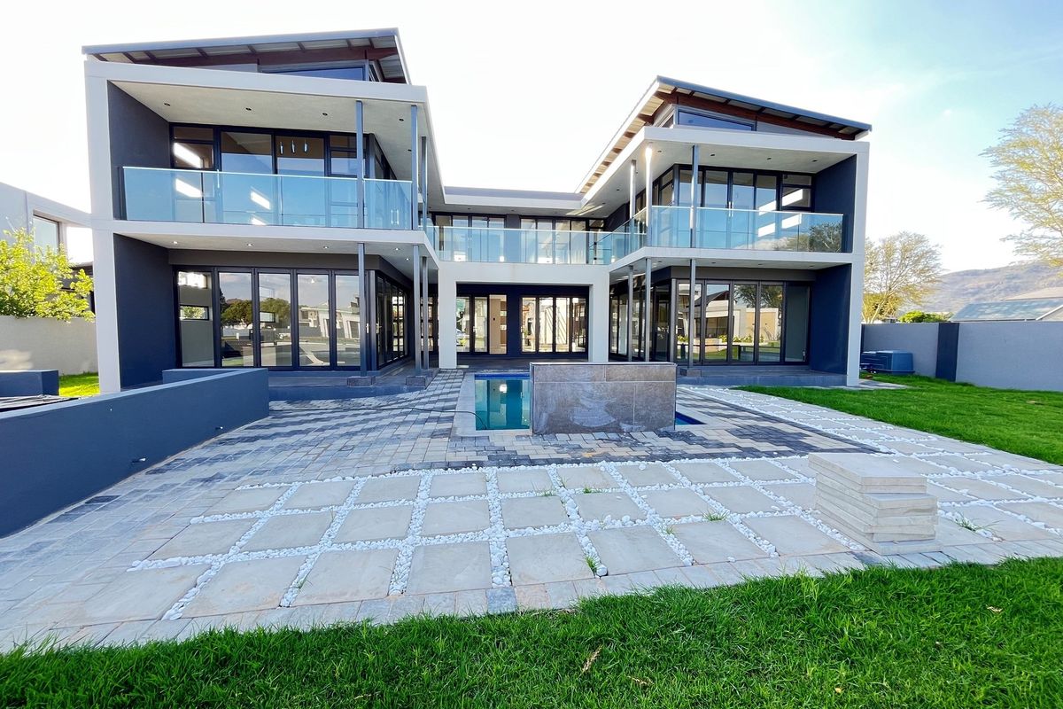Modern double-story residence featuring expansive glass facades, multiple balconies with glass balustrades, a paved patio area, and a central swimming pool.