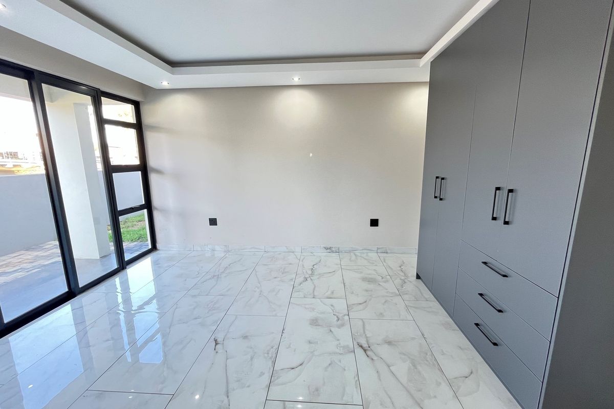 Modern bedroom featuring sleek grey built-in cupboards, polished marble-look floor tiles, recessed ceiling lighting, and large glass sliding doors leading to the exterior.