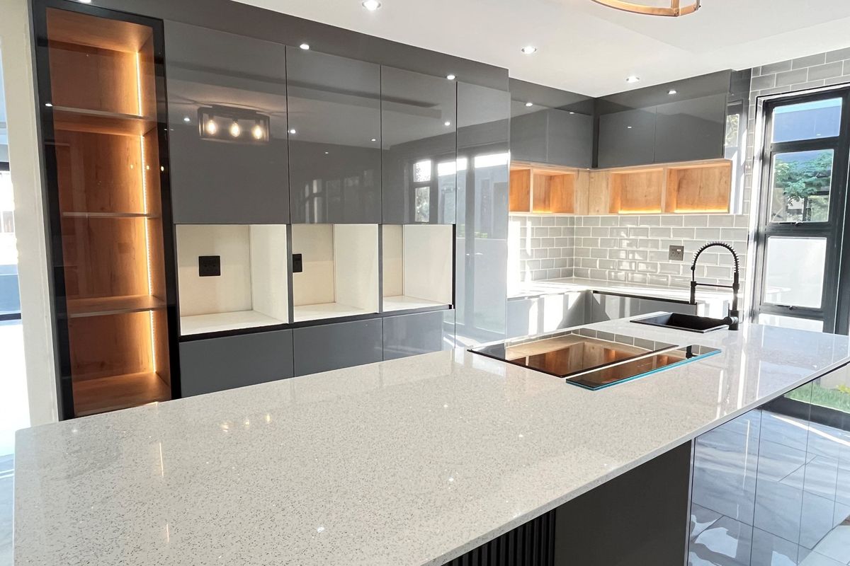 Modern kitchen featuring a large stone-topped island, sleek grey cabinetry, integrated lighting, and subway tile backsplash with a contemporary sink and faucet.