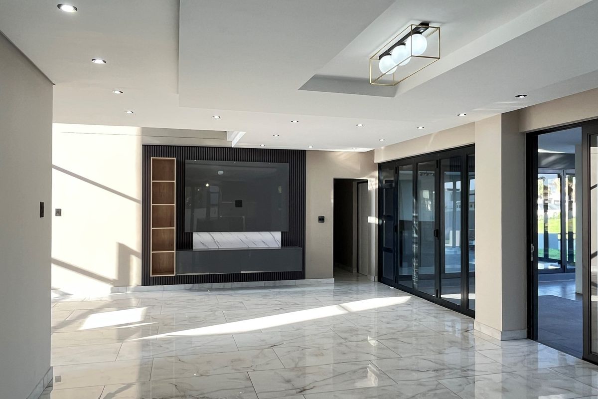 Modern living area featuring high-gloss marble-look floor tiles, a custom built-in media wall with shelving, recessed ceiling lighting, and large black-framed glass sliding doors.
