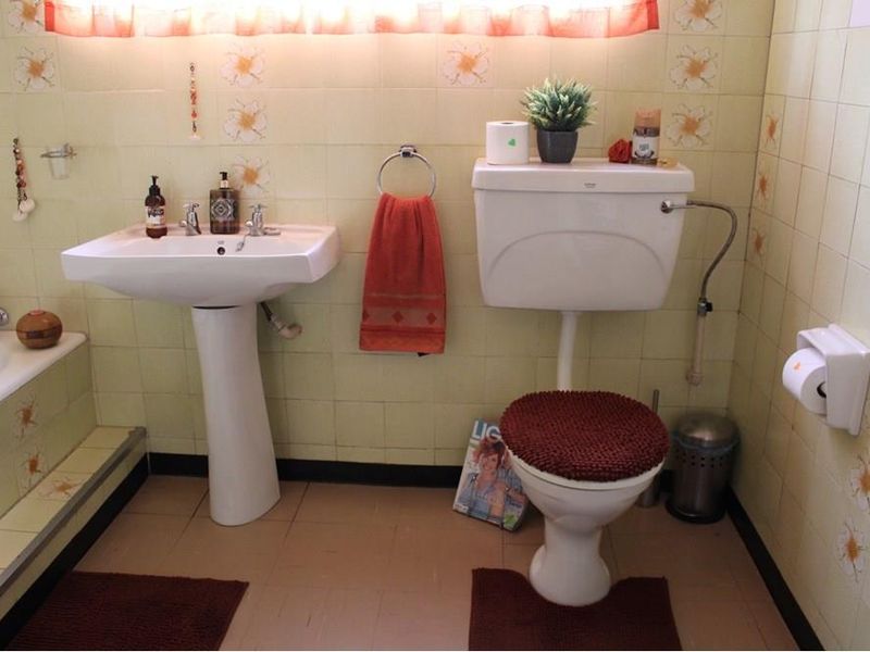 A dated bathroom featuring a pedestal basin, toilet, and bathtub with original floral-patterned wall tiles.