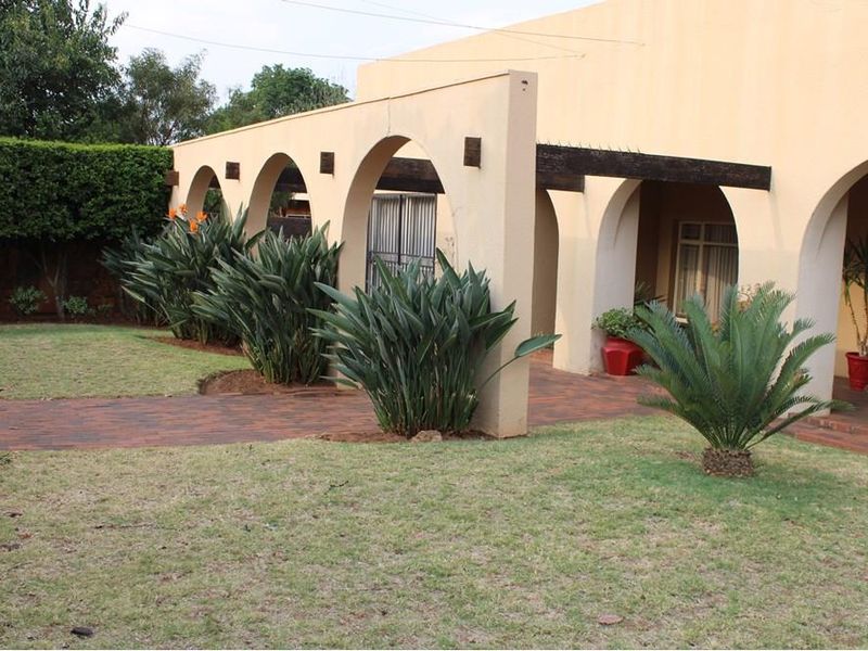 A well-maintained rear garden featuring a paved walkway, a manicured lawn, and a distinctive arched colonnade with timber pergola beams.