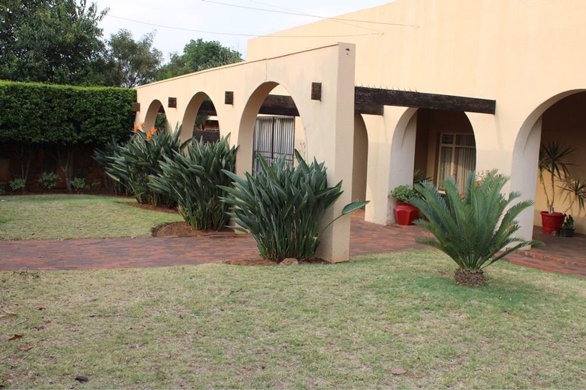 A well-maintained rear garden featuring a paved walkway, a manicured lawn, and a distinctive arched colonnade with timber pergola beams.