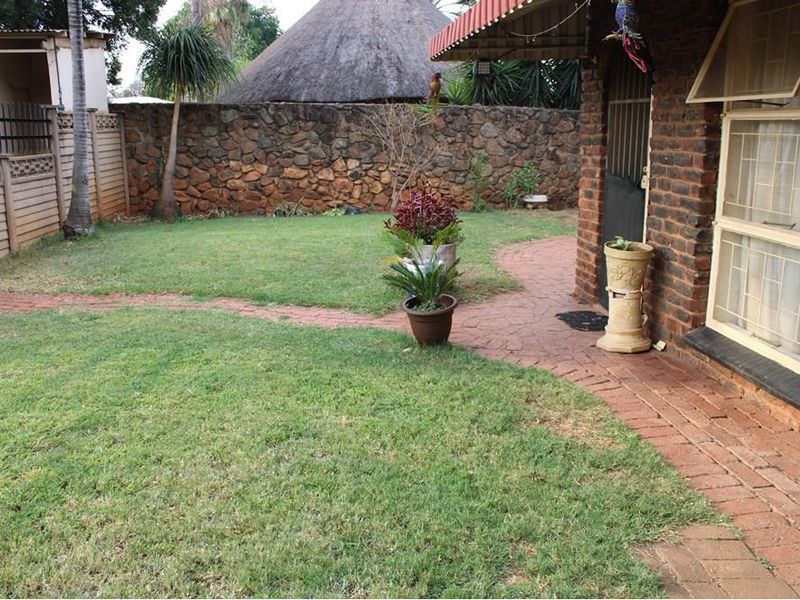 Rear garden area featuring a brick-paved walkway, stone boundary wall, and direct access to the house via a security gate.