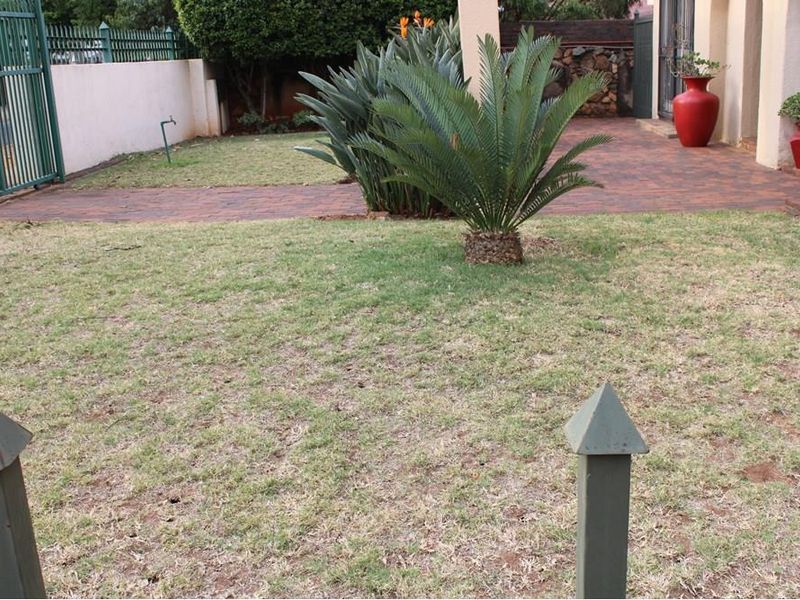 A front garden area featuring a paved walkway, boundary wall, metal gate, and established landscaping.