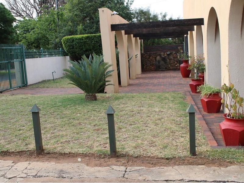 A covered patio area featuring arched pillars, a timber pergola, and brick paving, adjacent to a garden space with a stone feature wall.