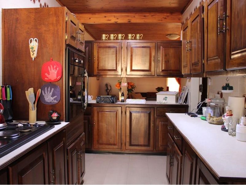 A traditional galley-style kitchen featuring extensive timber cabinetry, built-in oven, electric hob, and a warm timber-paneled ceiling.
