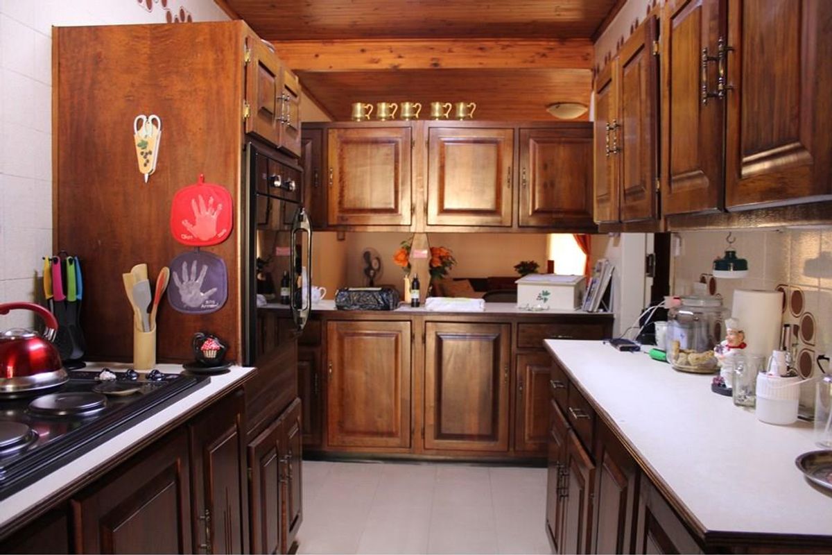 A traditional galley-style kitchen featuring extensive timber cabinetry, built-in oven, electric hob, and a warm timber-paneled ceiling.