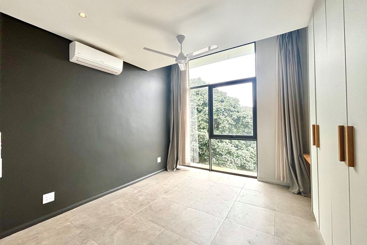 A bright bedroom featuring large windows, built-in cabinetry, a ceiling fan, and a wall-mounted air conditioning unit.