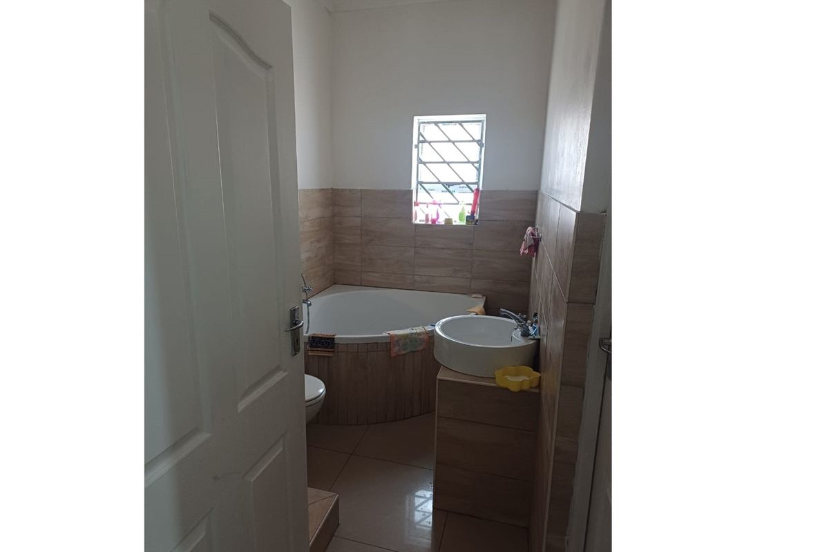 A compact bathroom featuring a corner bathtub, a vessel sink vanity, and tiled walls with a security-barred window.