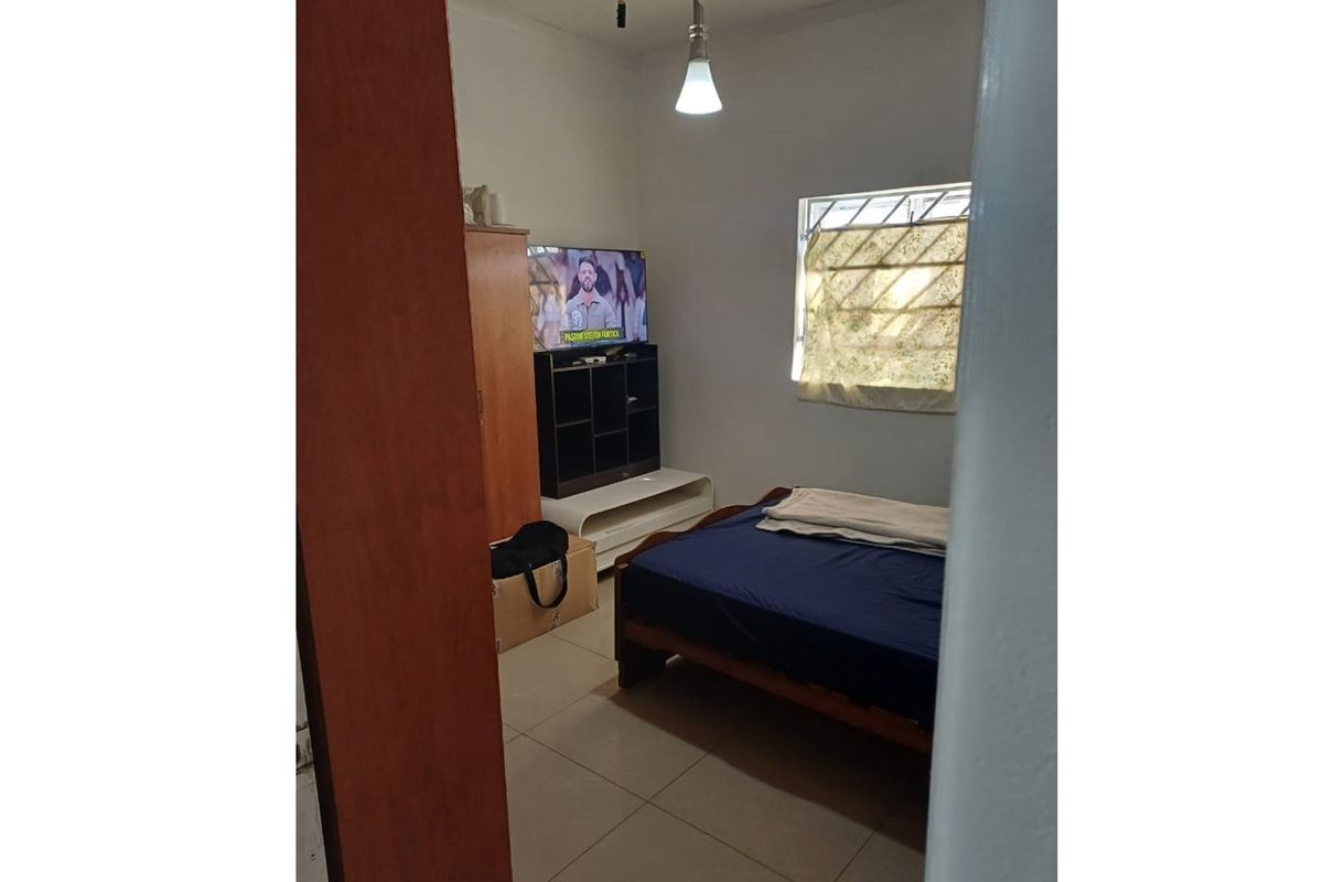 A standard bedroom featuring tiled flooring and a window with security bars, viewed from the doorway.