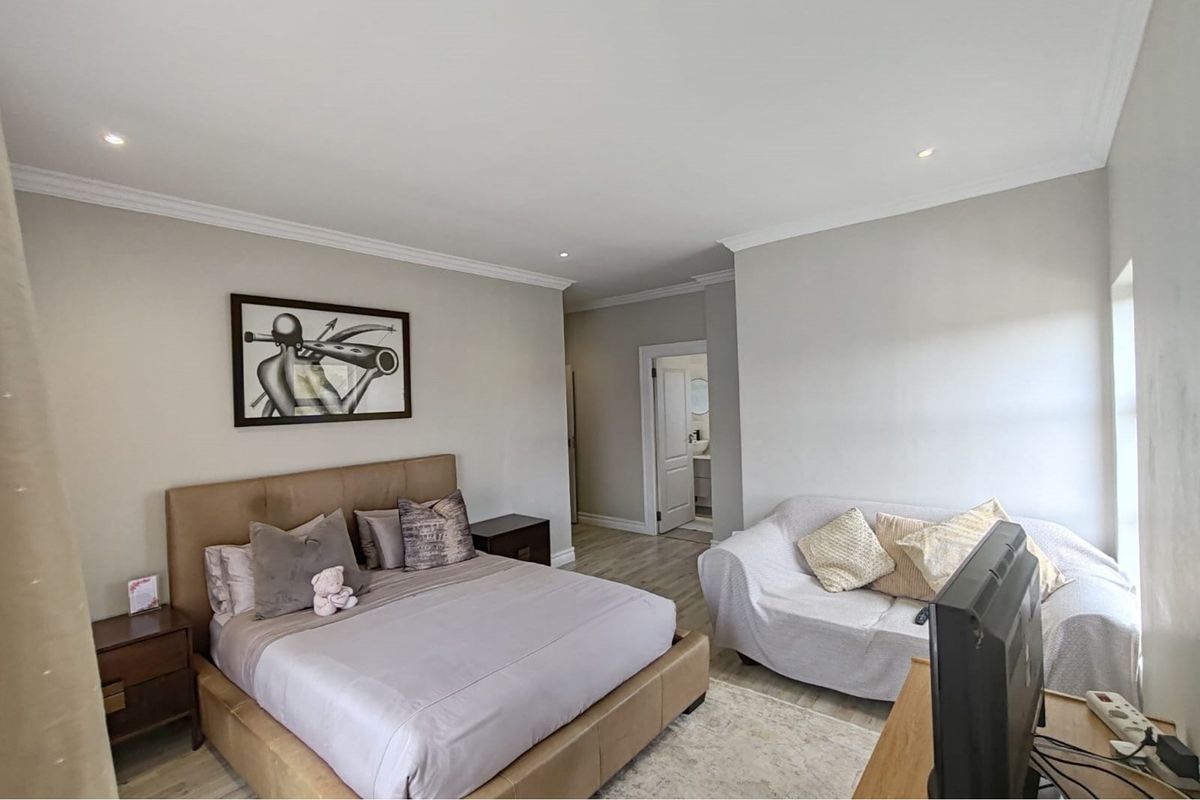 A well-maintained bedroom featuring neutral wall tones, recessed downlighting, decorative cove cornicing, and light-toned laminate flooring, with an adjoining en-suite bathroom visible.
