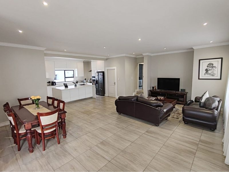 Spacious open-plan living area featuring a modern kitchen with island, tiled flooring, and recessed lighting, creating a seamless flow between dining and lounge spaces.
