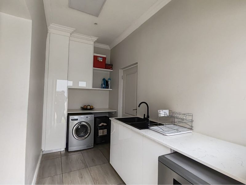 A modern, well-maintained laundry room featuring sleek white cabinetry, stone countertops, a black sink, and tiled flooring with integrated appliance space.