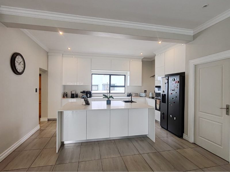 Modern kitchen featuring a central island, sleek white cabinetry, stone countertops, and tiled flooring with recessed lighting.