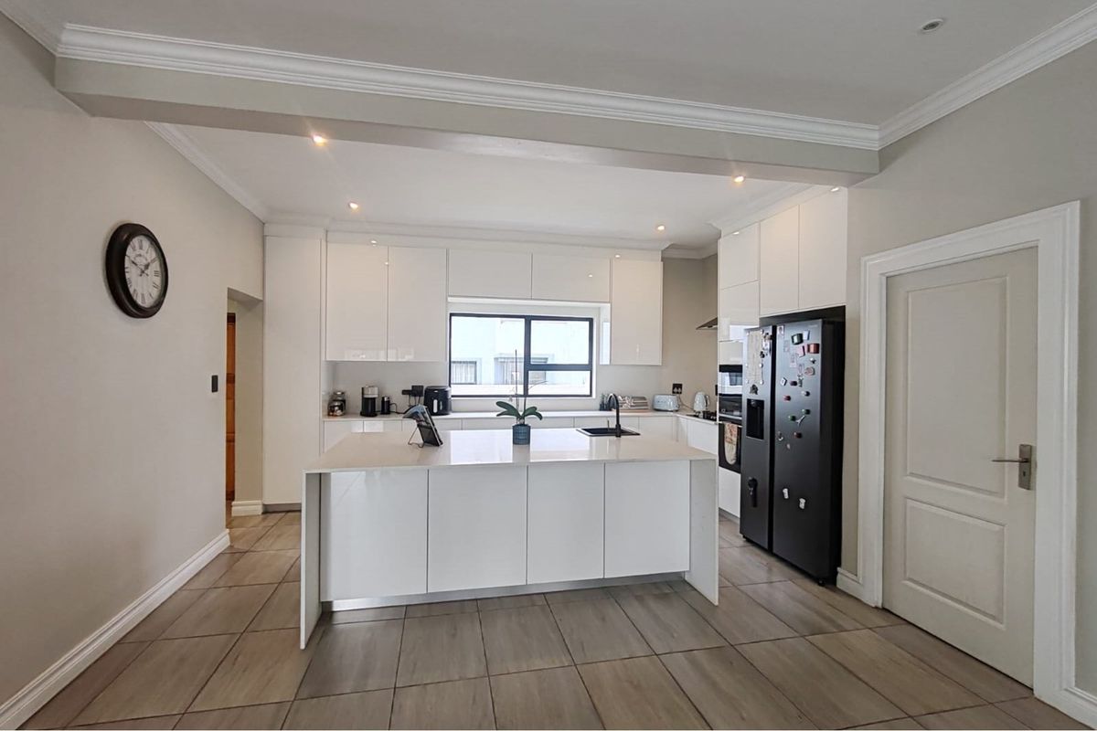 Modern kitchen featuring a central island, sleek white cabinetry, stone countertops, and tiled flooring with recessed lighting.