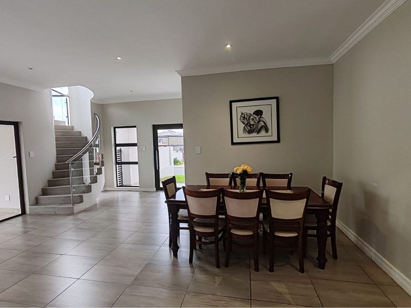 Spacious dining area featuring tiled flooring, recessed lighting, and a modern staircase with a glass balustrade, creating an open and bright atmosphere.