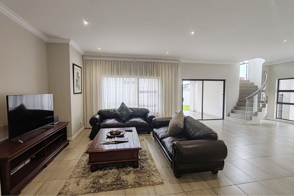 Spacious living room featuring neutral tiled flooring, recessed downlighting, and a modern staircase with a glass balustrade leading to the upper level.