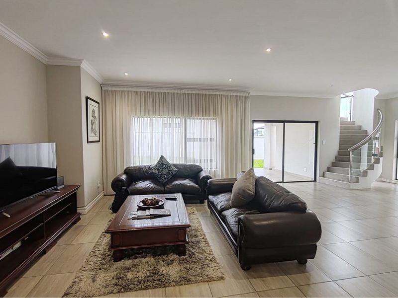 Spacious living room featuring neutral tiled flooring, recessed downlighting, and a modern staircase with a glass balustrade leading to the upper level.