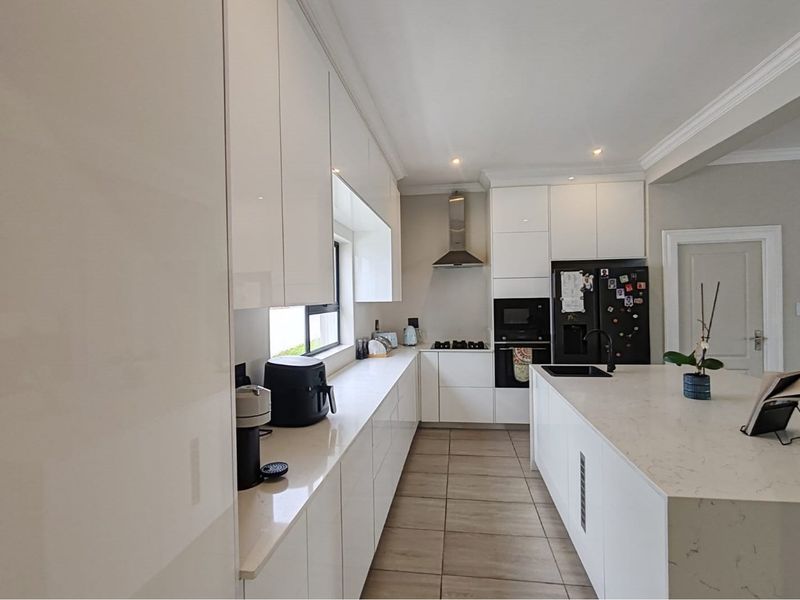 Modern kitchen featuring sleek white cabinetry, stone countertops, a central island with an undermount sink, and integrated appliances with recessed lighting.