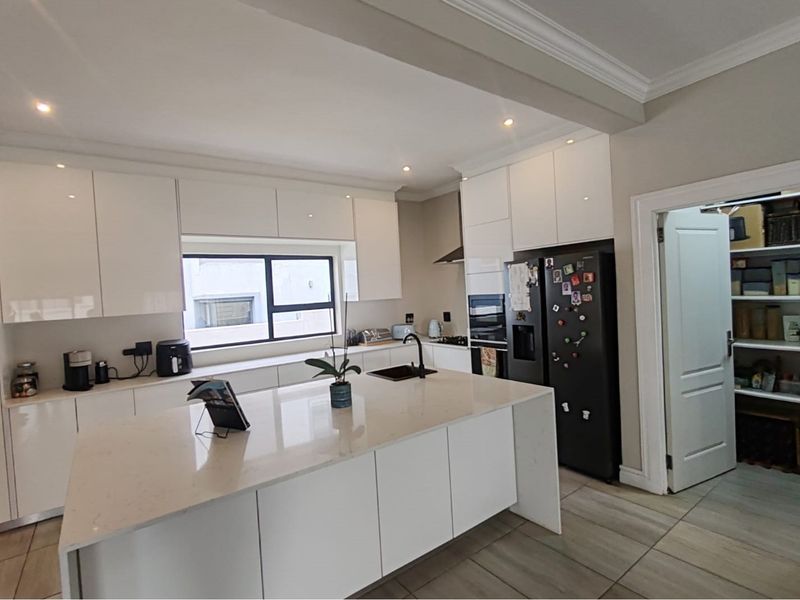 Modern kitchen featuring white high-gloss cabinetry, a large central island with quartz countertops, integrated appliances, and an adjacent walk-in pantry.