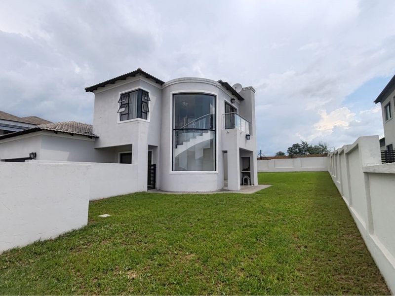 Rear view of a modern two-story house featuring a curved glass staircase facade, a balcony, and a spacious private garden with perimeter walling.