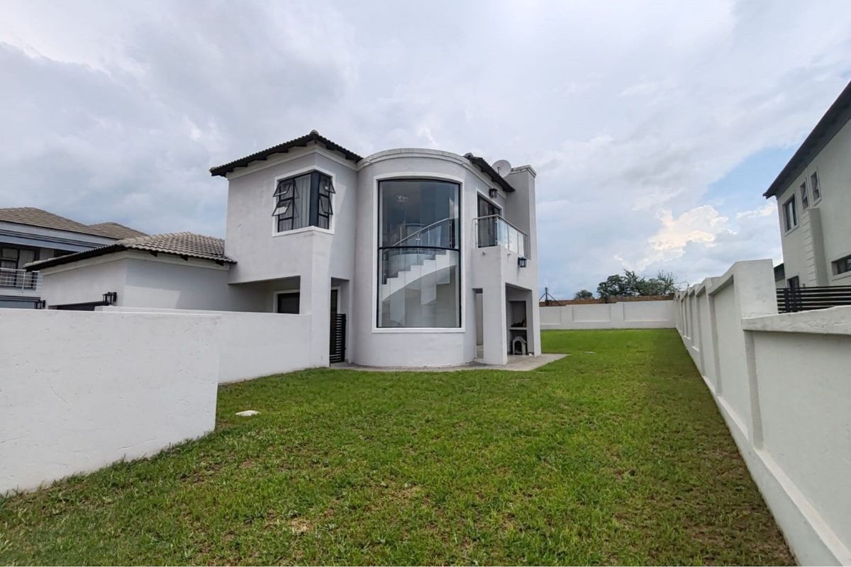 Rear view of a modern two-story house featuring a curved glass staircase facade, a balcony, and a spacious private garden with perimeter walling.