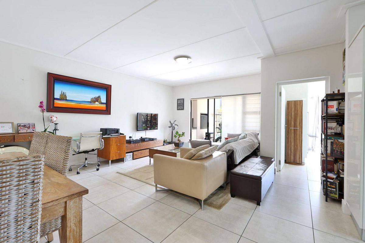 A bright and spacious living room featuring neutral tiled flooring, a ceiling light fixture, and a sliding glass door leading to an outdoor area.