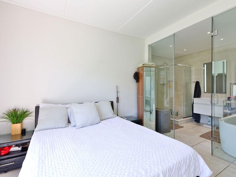 Modern bedroom featuring an open-plan en-suite bathroom with a glass partition, walk-in shower, vanity, and a contemporary freestanding bathtub.