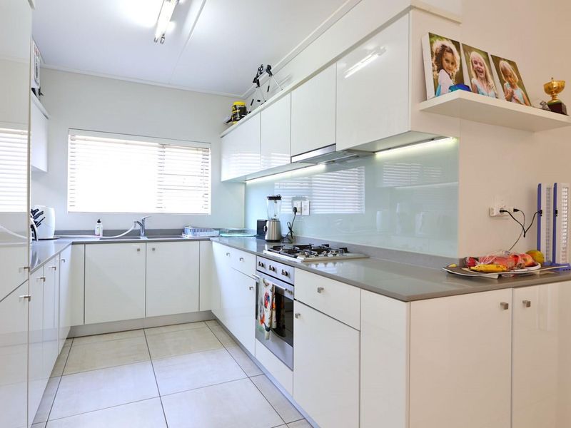 Modern kitchen featuring white high-gloss cabinetry, stone countertops, a gas hob, built-in oven, and a sleek glass splashback with under-cabinet lighting.