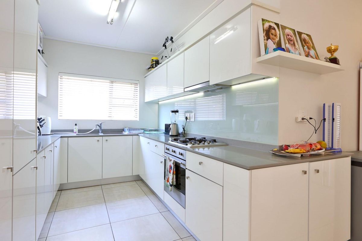 Modern kitchen featuring white high-gloss cabinetry, stone countertops, a gas hob, built-in oven, and a sleek glass splashback with under-cabinet lighting.