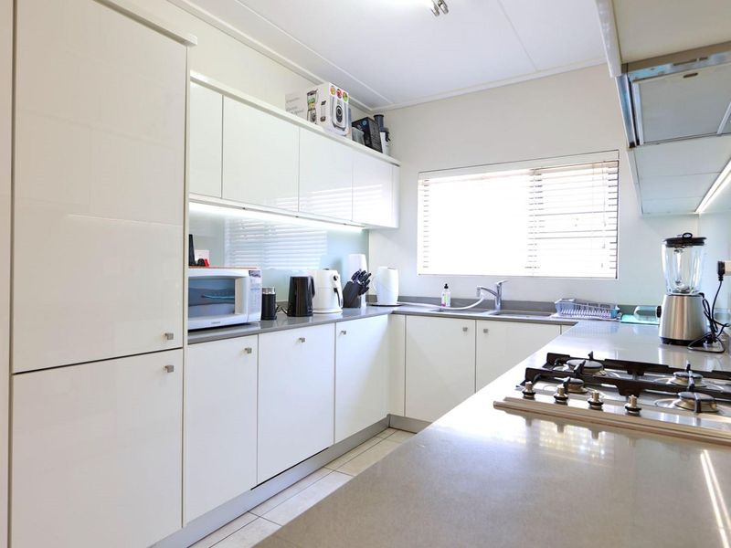 Modern kitchen featuring white high-gloss cabinetry, stone countertops, a gas hob with extractor fan, and a stainless steel sink with a window view.