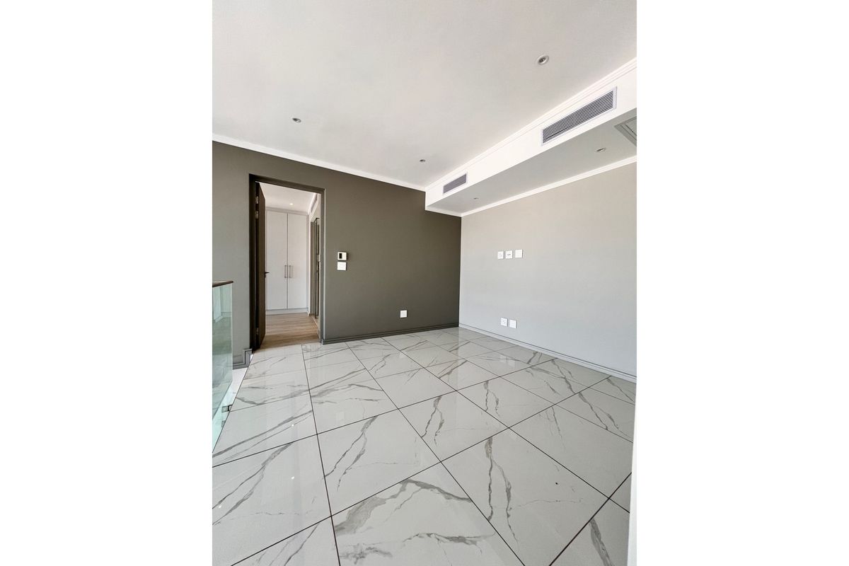 A bright, modern living area featuring large-format marble-look porcelain floor tiles, recessed ceiling lighting, and integrated ducted air conditioning.
