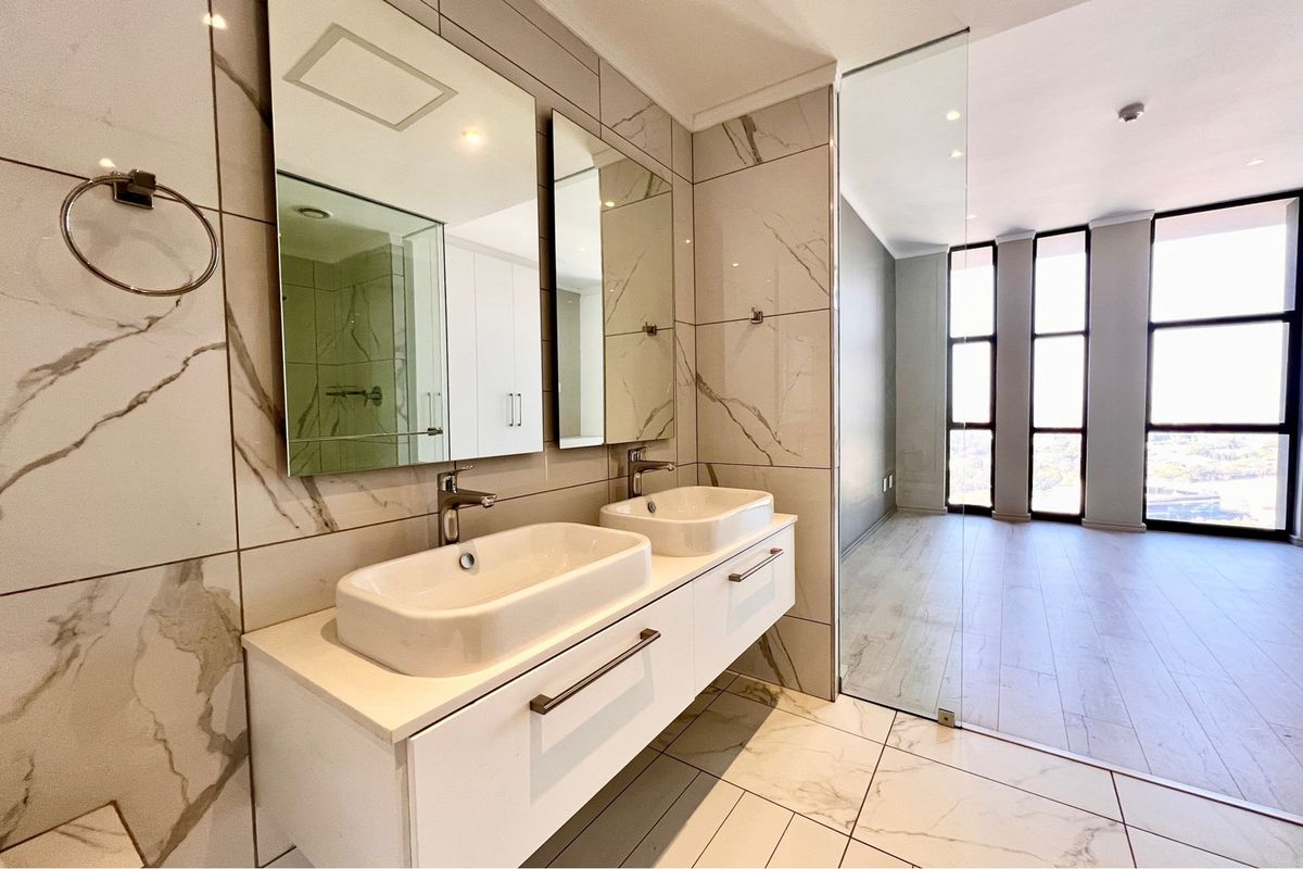 Modern bathroom featuring a double vanity with vessel sinks, marble-look wall tiles, and a glass partition separating the space from the adjacent room.